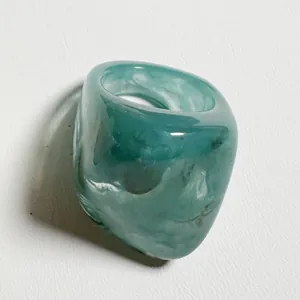 Detalle de un anillo de acrílico verde azulado translúcido con jaspeado blanco