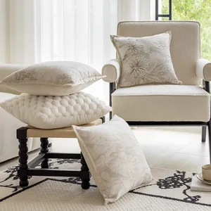 Detail of cream-colored textured and patterned decorative pillow covers on a cozy chair.