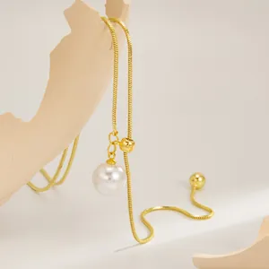 Detail van een gouden slangenketting met witte parelhanger en verstelbare kraal.