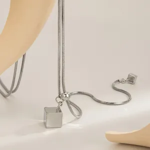 Detailopname van zilveren roestvrijstalen ketting met geometrische kubus hanger en slangenketting.