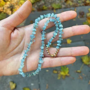 Vue détaillée d'un collier artisanal en pierres bleu clair irrégulières tenu dans la main