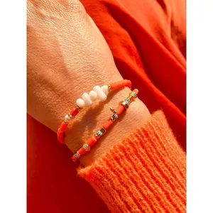 Macro view of bohemian orange handmade beaded bracelet set with shell accents on a wrist