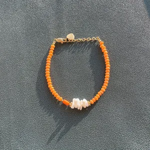 Detailed close-up of a bohemian handmade orange beaded bracelet with white shell chips.