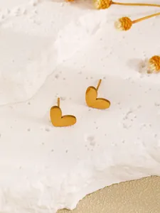 Macro view of gold heart-shaped stud earrings on white textured stone background