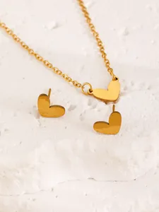 Close-up of gold heart pendant necklace and matching stud earrings on white stone set.
