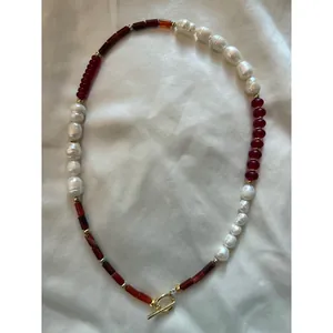 Detailed view of natural pearl and red stone beaded necklace with gold toggle clasp.