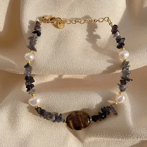 Primo piano di bracciale con occhio di tigre e perle su morbido tessuto crema