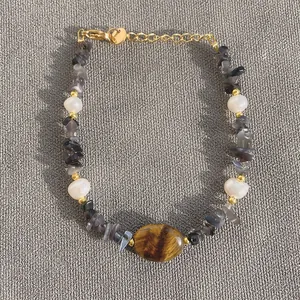 Vista dettagliata del bracciale con occhio di tigre e perle su tessuto grigio
