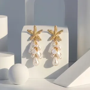 Makro-Detail von goldenen Seestern-Ohrringen mit kaskadierenden weißen Barockperlen.