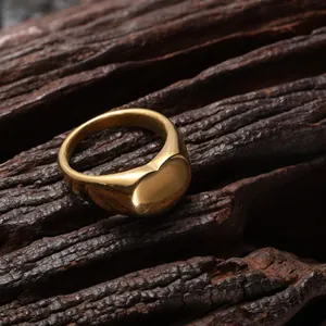 Primer plano de un anillo de corazón minimalista en acero dorado sobre fondo rústico