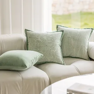 Set of sage green decorative pillows with floral embroidery on a modern white sofa