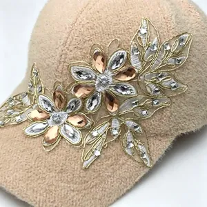Dettaglio cappello baseball beige in peluche con ricamo floreale in strass lucidi.