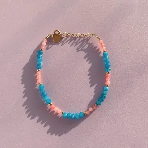 Close-up of bohemian colorful natural stone beaded bracelet with heart charm on purple background