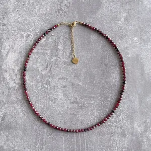 Détail d'un collier artisanal avec des perles facettées en pierre naturelle rouge foncé.