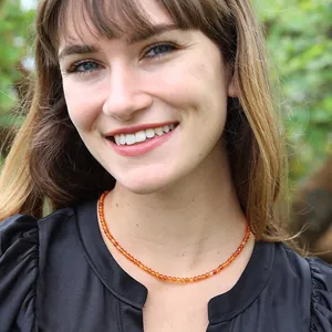 Vue détaillée d'un collier artisanal en perles de pierre orange porté par une femme souriante