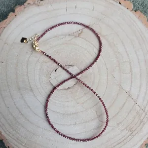 Détail d'un collier de perles en pierre naturelle rouge foncé sur fond de bois brut