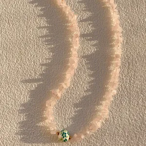 Gros plan sur un collier de pierres concassées roses de style bohème avec perle verte