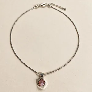 Gros plan d'un collier en argent avec un pendentif rond en calcédoine rose sur fond texturé.