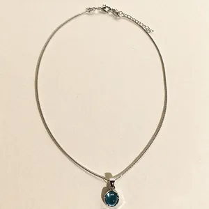 Collier argenté élégant orné d'un pendentif bleu rond poli sur une fine chaîne en serpent.