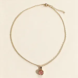 Vue détaillée d'un collier en chaîne dorée avec pendentif rond en calcédoine rose sur fond uni.