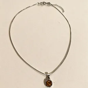 Vue détaillée d'un collier en argent avec pendentif œil de tigre sur un fond beige