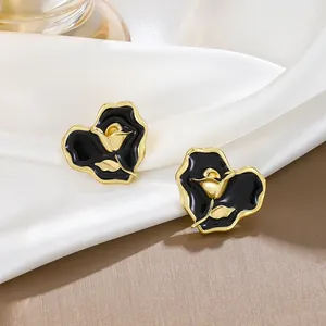 Detail view of heart-shaped black enamel stud earrings with gold rose motif