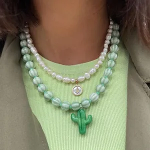 Gros plan de colliers superposés en verre et perles avec un pendentif en forme de cactus