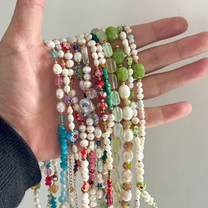 Détail de colliers artisanaux colorés en verre millefiori et perles, tenus dans une main