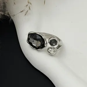 Détail d'une bague en argent texturé avec une grande pierre facettée en acrylique noir.