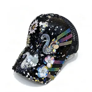 Detalle de gorra de lentejuelas con cisne de diamantes y parches de flores en fondo blanco.