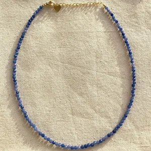 Close-up detail of blue natural stone beaded necklace with gold heart charm on linen