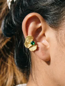 Close-up view of golden gingko leaf ear cuff with a green gemstone on a model's ear