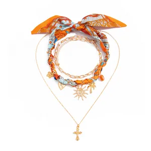Lagen-Goldkette mit orangefarbenem Schal und tropischen Anhängern im Detail