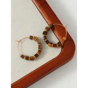 Detail of vintage gold hoop earrings with brown cubic tiger's eye stones on a wooden tray.
