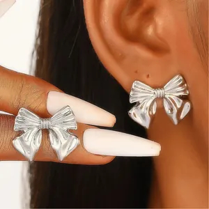 Close-up detail of silver-toned bow earrings showing intricate textured metal design.