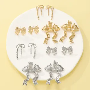 Detailed collection of gold and silver bow-shaped stud and drop earrings on a white plate.