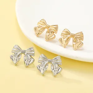 Close-up of elegant gold and silver bow stud earrings displayed on a minimalist background
