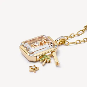 Detalle de collar de medallón de vidrio chapado en oro con dijes de LOVE y palma.
