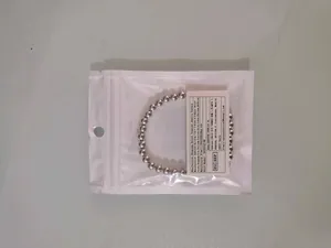 Detail view of silver metallic beaded elastic bracelet inside its retail packaging with label.