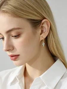 Gros plan d'un mannequin portant des boucles d'oreilles croix dorées et zircons bleus