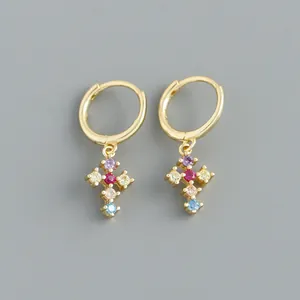 Détail macro de boucles d'oreilles créoles dorées avec pendentifs croix en zircon.