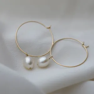 Gros plan de boucles d'oreilles créoles en acier titane doré avec perles naturelles.