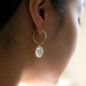 Détail d'une boucle d'oreille en perle baroque naturelle avec anneau doré sur modèle