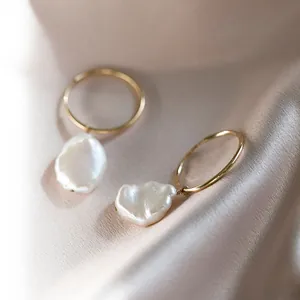 Détail de boucles d'oreilles en perles baroques et anneaux dorés sur fond de soie élégant.