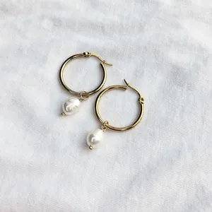 Vue détaillée de créoles dorées avec pendentifs en perles baroques sur tissu blanc.