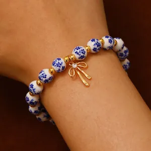 Bracciale di perle in ceramica stile porcellana bianca e blu con fiocco dorato.