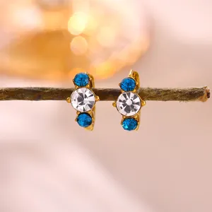 Close-up of elegant gold-tone hoop earrings with blue and clear zircon stones.