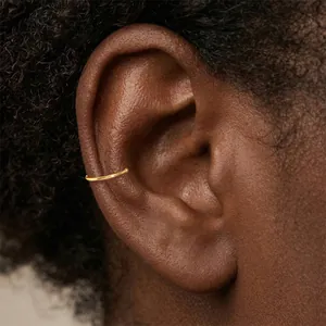 Gedetailleerde close-up van een minimalistische vergulde zilveren ear cuff op het oor.