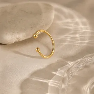 Elegante gouden open oorring met bolletjes tegen een zachte zandachtergrond met golven.