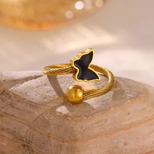 Detalle de cerca de un anillo dorado con banda trenzada y un diseño de mariposa negra sobre piedra.